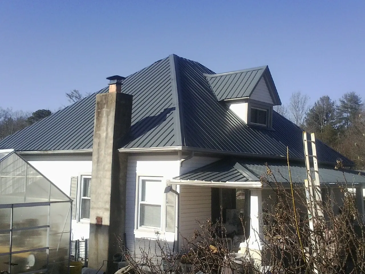 Dark blue standing seam metal roof on a white farmhouse with dormer — Slate & Tile Roof Repair by Roofing Brothers in Brook Park