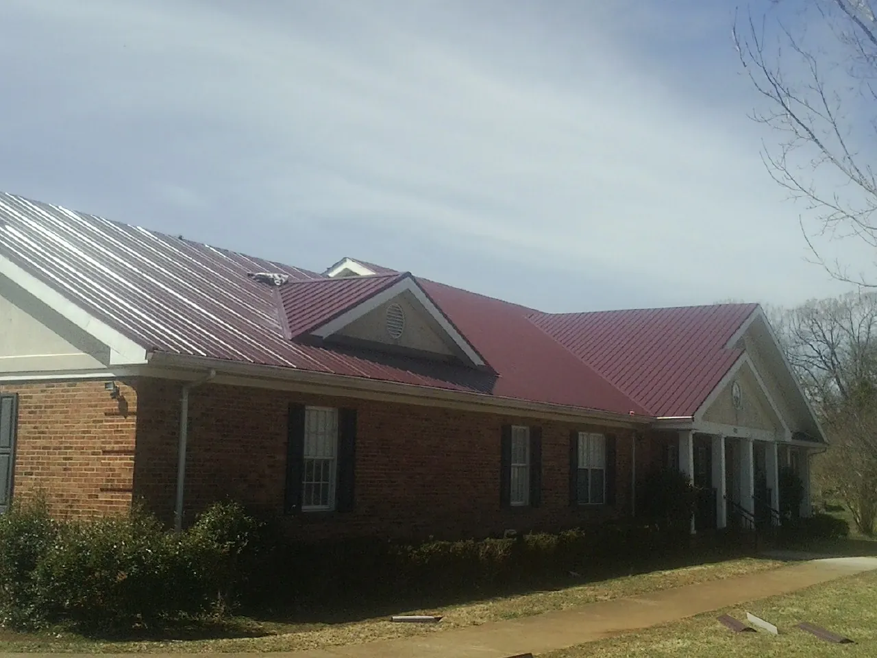 Red metal roof with gabled entries on a long brick building, from a Hail Damage Roof Repair job in Brook Park