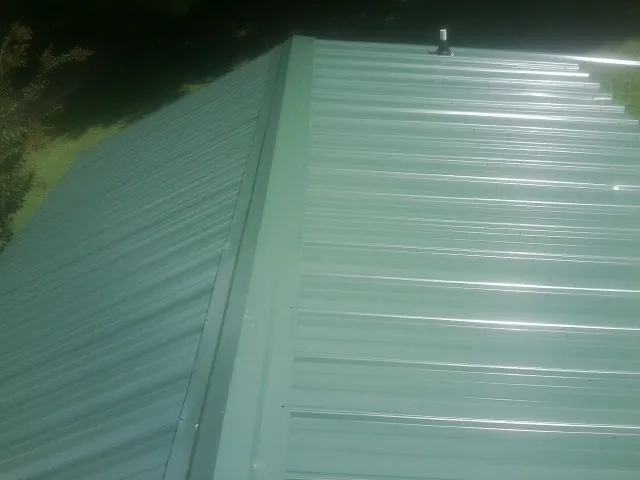 New green metal panels meeting at the ridge of a roof — Flat Roof Repair work by our crew in Brook Park