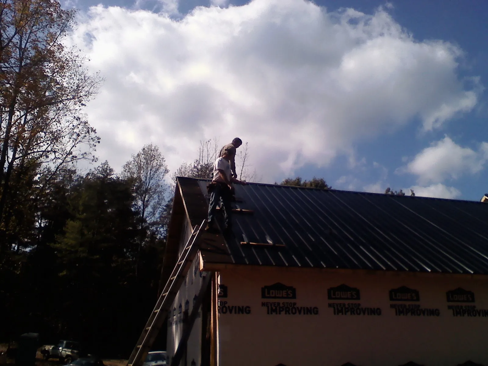 Roofer fastening dark metal panels high against a cloudy sky, from a Roof Inspection job in Brook Park