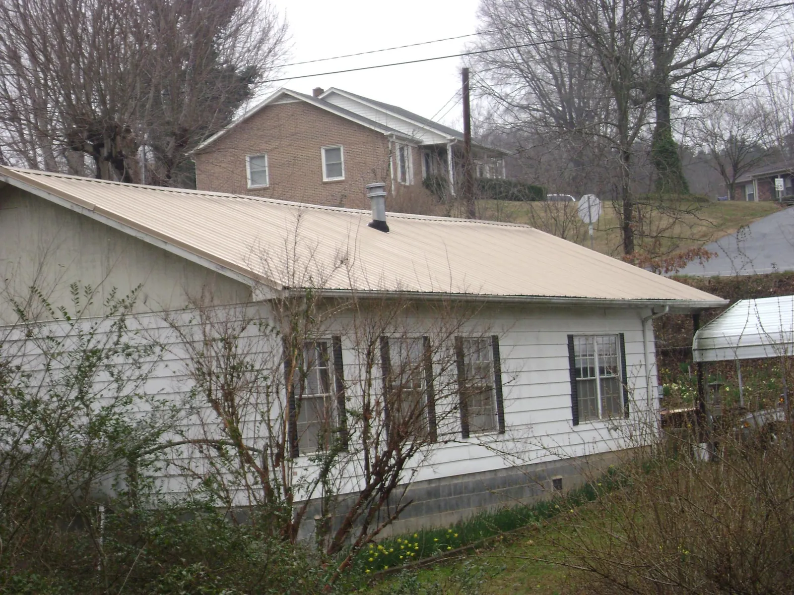 Tan metal roof on a white sided house set into a hillside — Commercial Roofing by Roofing Brothers in Brook Park